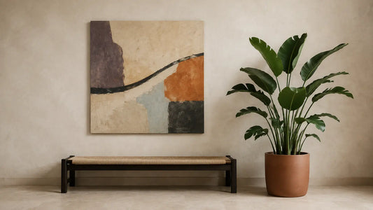 Original square abstract canvas beside a broad-leaf indoor plant above a low blackened-oak bench on a warm mineral wall